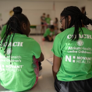 Two Girls on the Run junior coaches sit with their backs to the camera in green shirts talking to each other